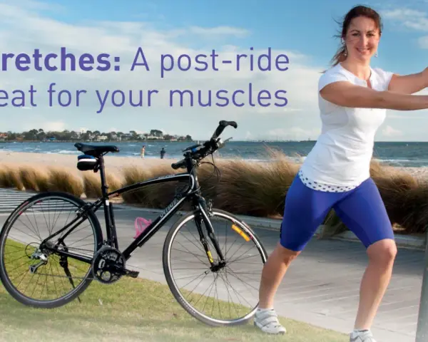 A woman performs a bicycle stretch, leaning on a pole after a ride by the beach.