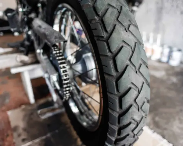 Zbliżenie na bieżnik motocyklowej opony, gotowej do wymiany. W tle widać fragment motocykla i narzędzia.