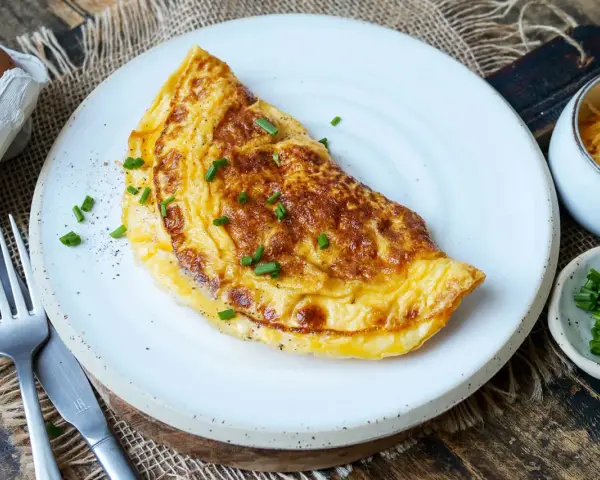 Goldbraunes Omelett mit Käse und Schnittlauch, perfekt für ein schnelles Omelette Rezept. Daneben Eier, Käse und Schnittlauch.