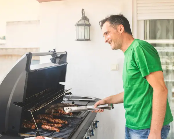 Glad man grillar korv på balkong.