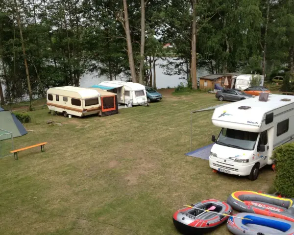 Campingplatz am sonnensee flachslanden mit Wohnmobilen, Wohnwagen, Zelt und Schlauchbooten am Ufer.