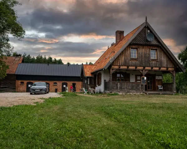 Szelągówka camping: drewniane domki i budynki gospodarcze, samochód na żwirowym podjeździe, zachmurzone niebo.