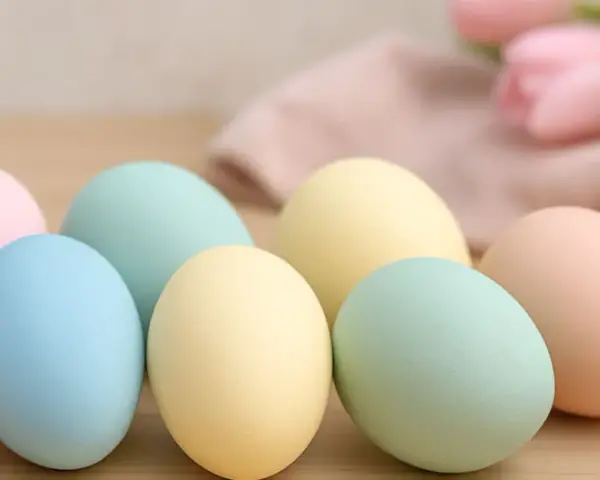 Huevos de pascua para pintar en tonos pastel, listos para decorar. Flores y tela suave al fondo.