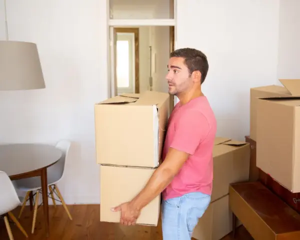 Un homme porte des cartons, prêt à quitter le domicile conjugal. Le propriétaire semble pensif, entouré de cartons de déménagement.