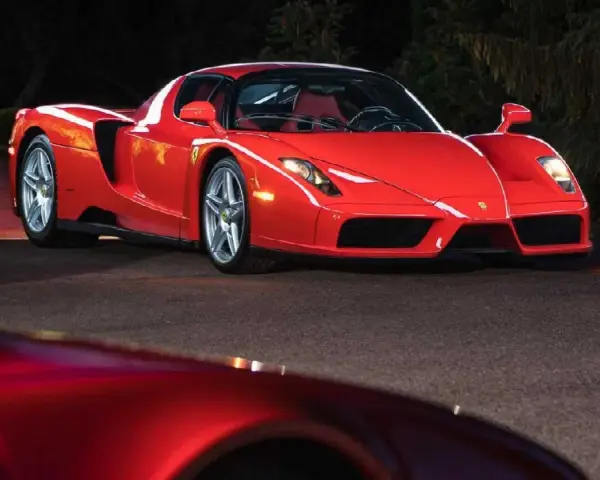 Czerwone Ferrari Enzo zaparkowane nocą na drodze, z innym czerwonym samochodem w tle.