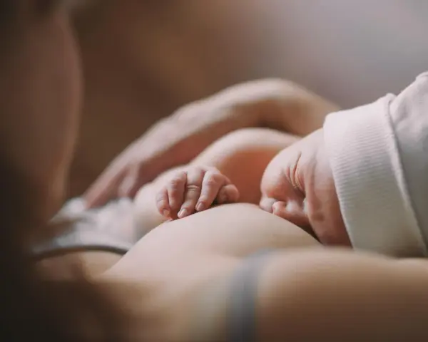 Ein Baby stillt, die kleinen Finger greifen sanft zu. Ein Moment der Ruhe und Verbundenheit.