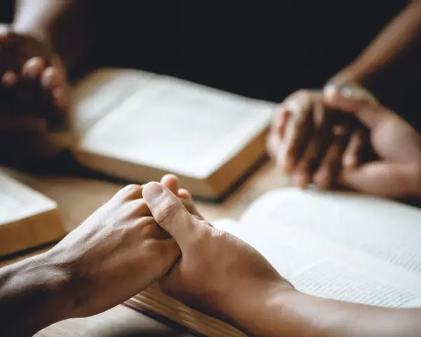 Hände halten sich über aufgeschlagenen Bibeln, ein Zeichen dafür, wie beten Christen: in Gemeinschaft, mit Glauben und Hoffnung.