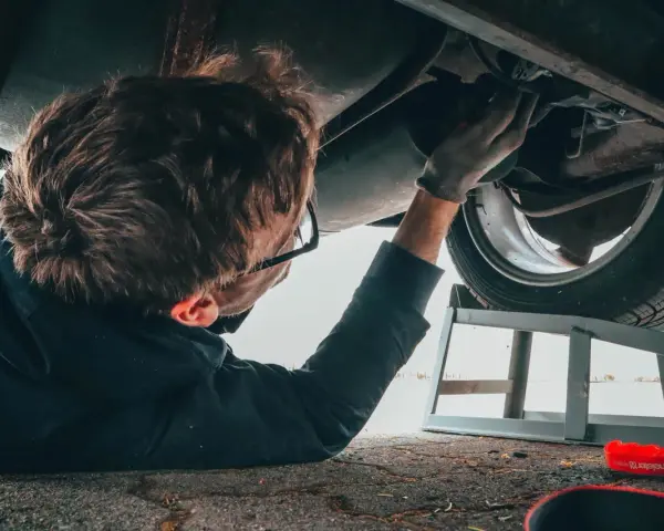 Un giovane impara come si diventa meccanico, lavorando sotto un'auto con attrezzi e spray.