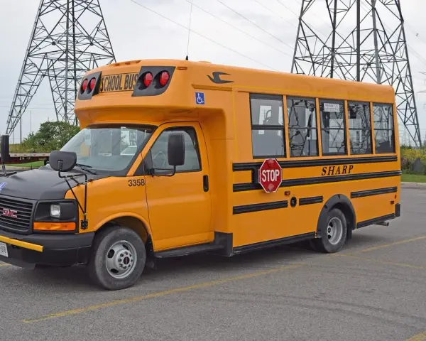 Żółty autobus szkolny GMC z napisem "SHARP" i znakiem STOP. Zastanawiasz się, ile kosztuje autobus?
