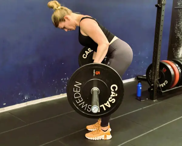 Kvinna utför en t bar row med en skivstång i ett gym.