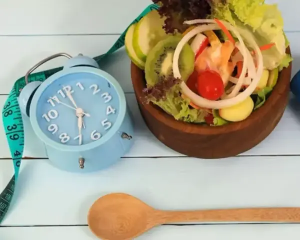 Réveil bleu, ruban à mesurer, salade fraîche et haltère bleu. L'heure est à la forme, jeune 16/8.