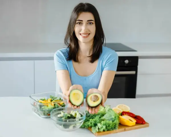 Uśmiechnięta kobieta prezentuje awokado, składnik wielu diet, w tym keto. Jej opinie o keto diecie są pozytywne.