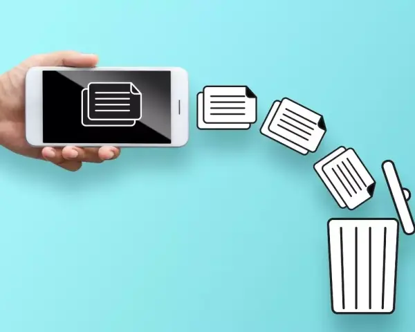 Dłoń trzyma telefon, z którego wypadają dokumenty prosto do kosza. Tak właśnie działa kosz w telefonie, gdy usuwasz pliki.