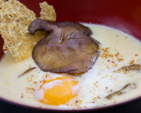 Un œuf parfait, crémeux et onctueux, baigne dans une soupe onctueuse, garnie d'un champignon poêlé et d'une tuile croustillante.