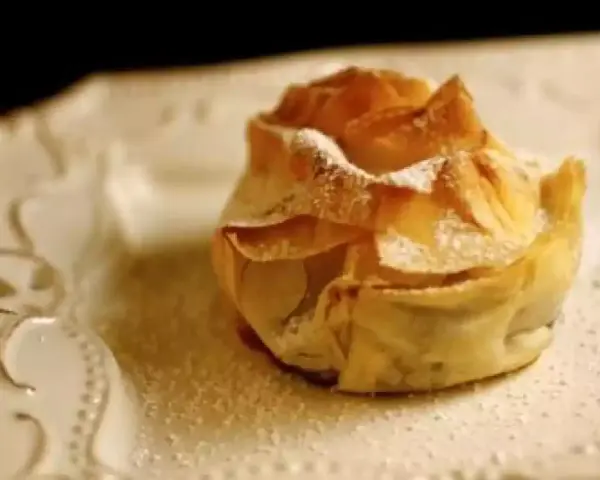 Delicioso saquito de pasta filo relleno de queso, espolvoreado con azúcar glas sobre un plato blanco.
