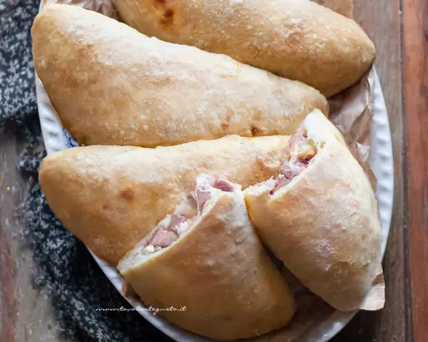 Calzoni al forno dorati e fragranti, ripieni di prosciutto e formaggio filante, pronti per essere gustati.