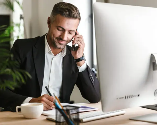 Uomo d'affari al telefono, scrive appunti. Potrebbe essere un agente immobiliare che discute di quanto guadagna un agente immobiliare.