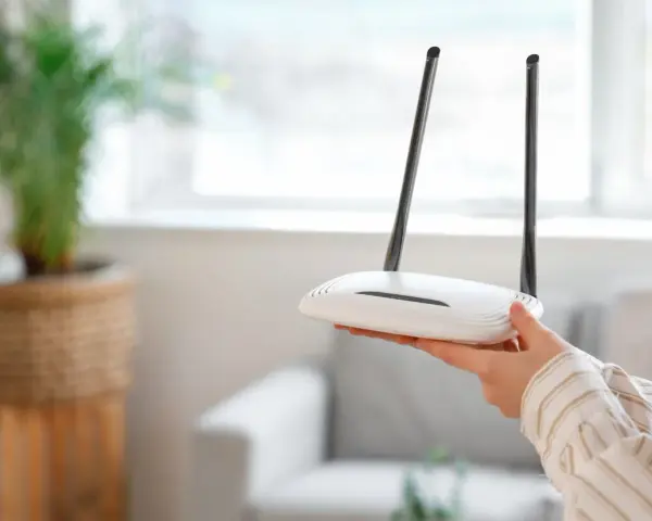 Dłoń trzyma biały router z dwiema antenkami. Dowiedz się, jak zresetować router, aby rozwiązać problemy z siecią.