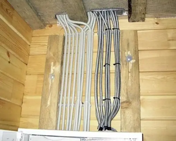 Instalacja elektryczna w domu drewnianym schemat: wiązki kabli w peszlach wychodzące z sufitu, przymocowane do drewnianych belek.