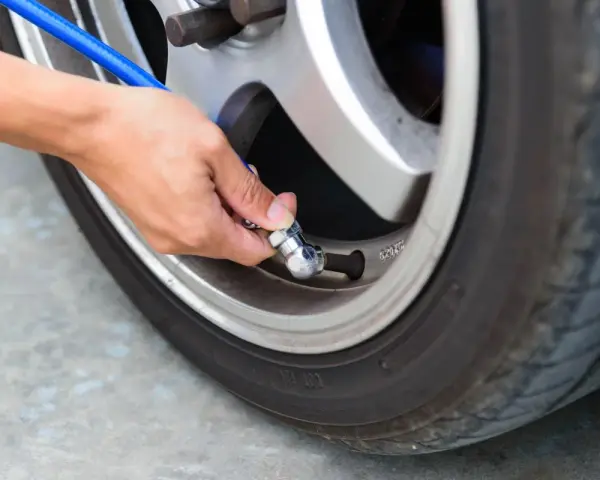 Mano che collega un tubo blu alla valvola di un pneumatico per controllare la pressione gomme auto.