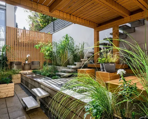 Giardini fioriti idee: un angolo zen con vasca d'acqua, gradini in pietra, sedute in legno e piante rigogliose sotto un pergolato.