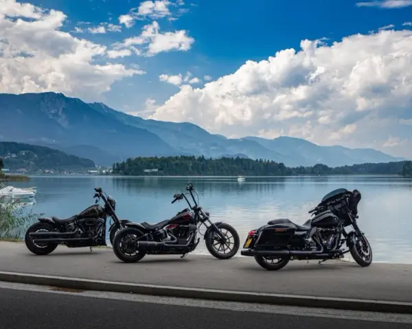 Tre moto parcheggiate sul lungolago, pronte per il faaker see motoraduno. Montagne sullo sfondo, cielo azzurro con nuvole bianche.