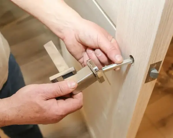 Hands assembling a modern door handle. A metal spindle is being inserted into the door mechanism, showing how to replace door handle.