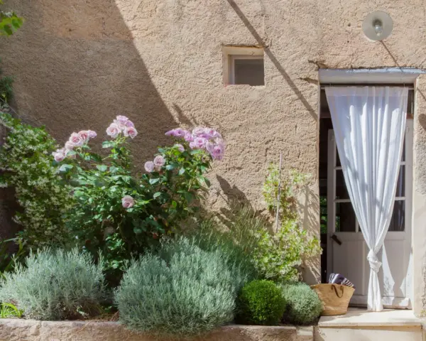 Lavendel beet ideen: Ein mediterraner Garten mit Rosen, Lavendel und einer Tür mit weißem Vorhang.