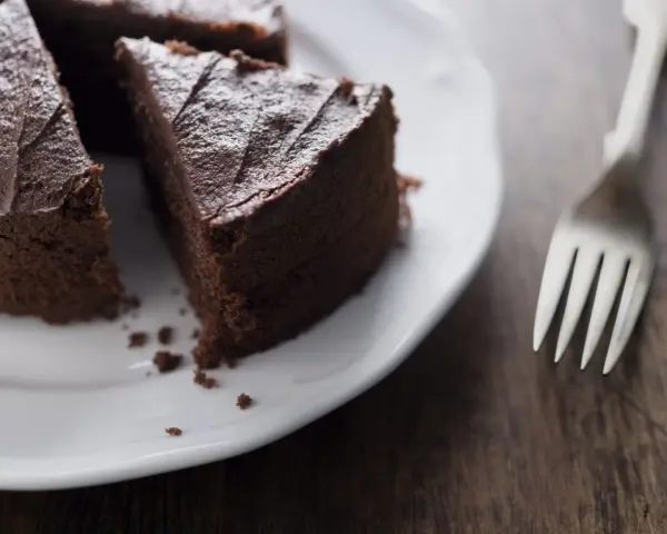 Una fetta di torta al cioccolato su un piatto bianco, con una forchetta accanto. Un'opzione deliziosa per chi cerca dolci senza zucchero.