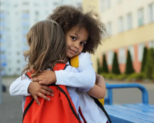 Zwei Kinder umarmen sich. Ein Mädchen mit Locken lächelt in die Kamera. Ein schönes Beispiel für Empathie bei Kindern.