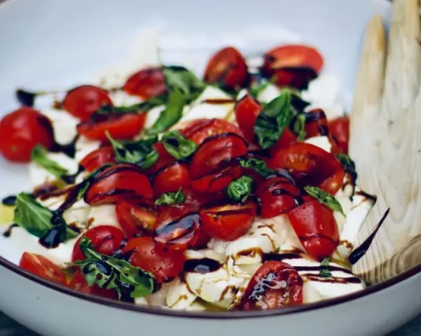 Frische Insalata Caprese mit saftigen Tomaten, cremigem Mozzarella und Basilikum, beträufelt mit Balsamico.