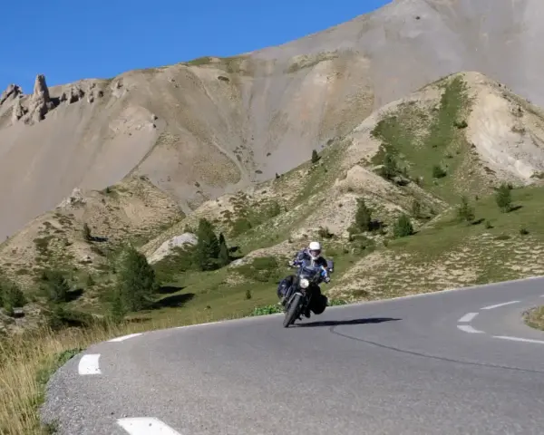Motociclista percorre la route de grand alpes tra montagne scoscese e cielo azzurro.