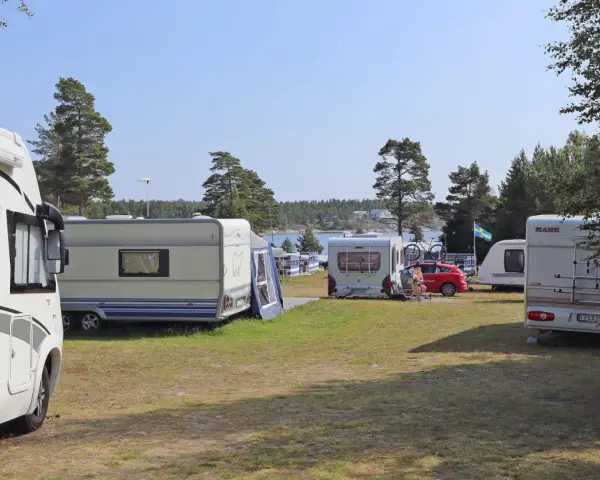 Solig dag på camping norrlandskusten med husbilar och husvagnar uppställda nära vattnet.