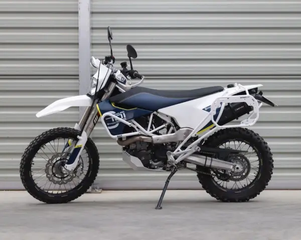 Biało-niebieski motocykl Husqvarna z bagażnikiem, gotowy na przygody w terenie. To idealny sprzęt do lekkiego enduro.