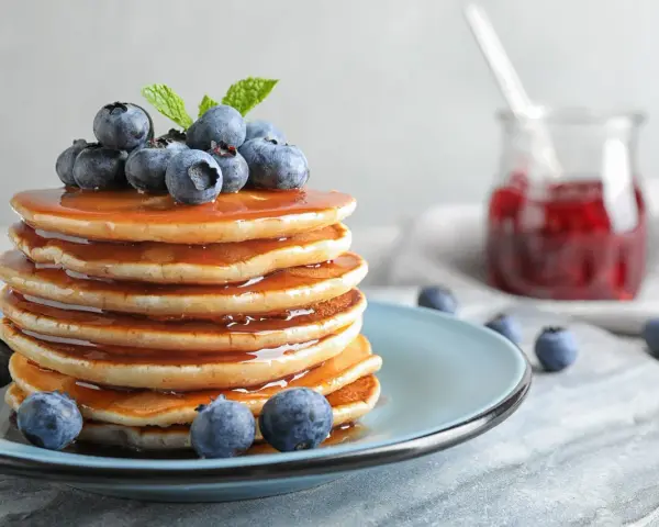 Stos puszystych pancakes polanych syropem, ozdobiony jagodami i miętą. Idealny przepis na pancake na śniadanie.