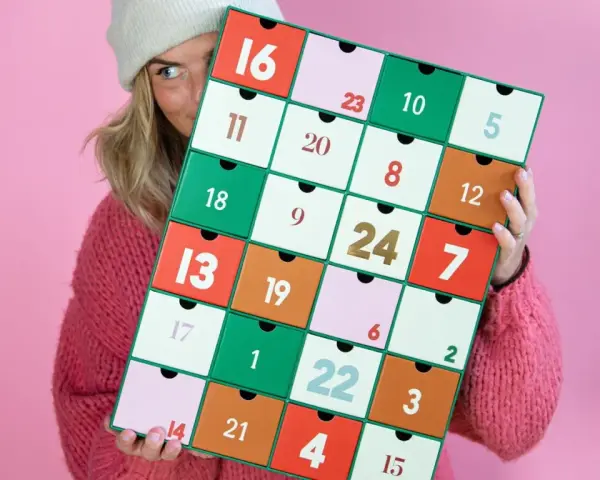 En person med en stickad tröja och mössa håller upp en färgglad julkalender. En perfekt julkalender diy att skapa själv!