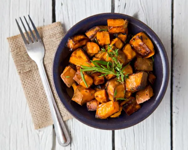Patate douce air fryer croustillante, garnie d'herbes fraîches, servie dans un bol bleu avec une fourchette.