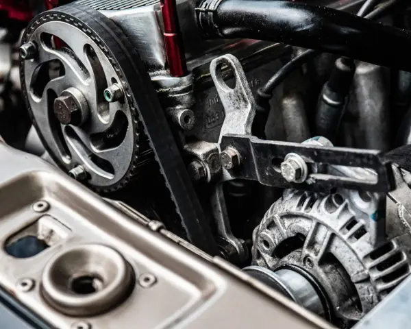 Close-up of a car engine showing a toothed drive belt wrapped around a pulley and connected to an alternator.