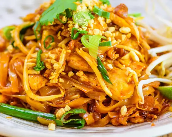 Un delicioso plato de pad thai con fideos de arroz, pollo, brotes de soja, cacahuetes picados y cilantro fresco.