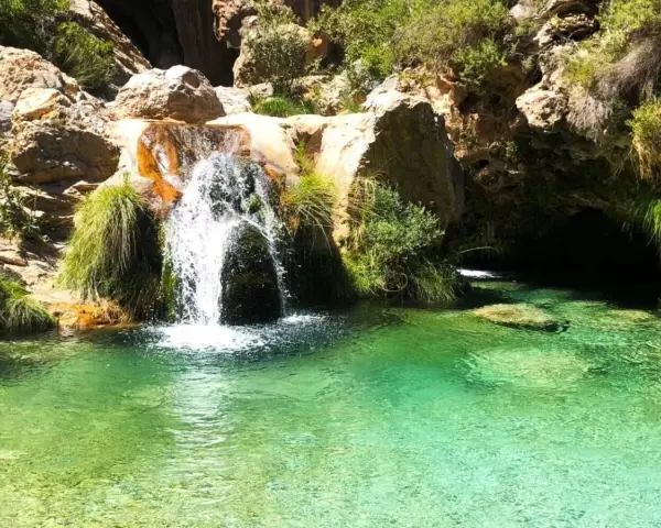 Cascada de agua cristalina cayendo en unas pozas turquesas, rodeadas de rocas y vegetación exuberante.