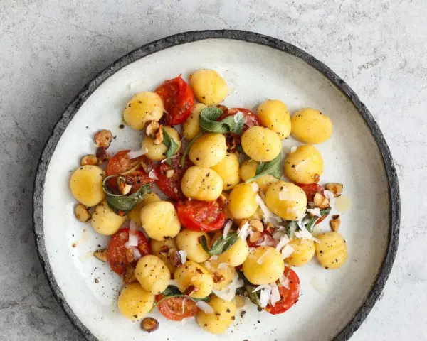 Pyszne makaron gnocchi z pomidorkami, szałwią i orzechami na talerzu.