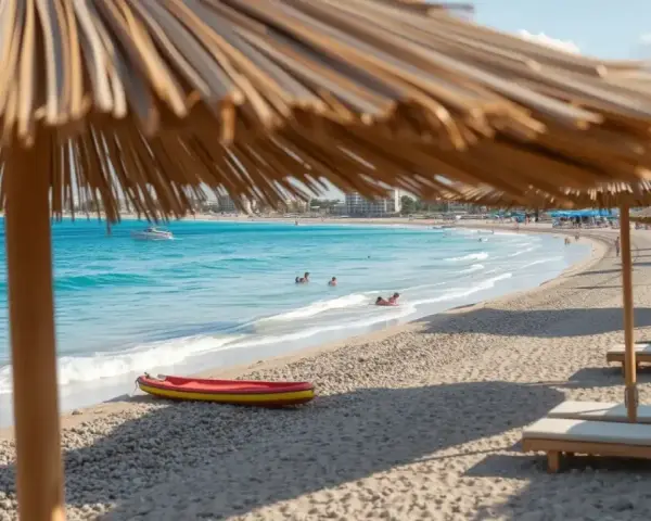 Słoneczny dzień na plaży Nissi Beach. Leżaki pod parasolami, turkusowa woda, kajak i ludzie kąpiący się w morzu.