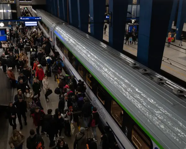 Tłum ludzi z bagażami na peronie kolejowym, wsiadający do pociągu.
