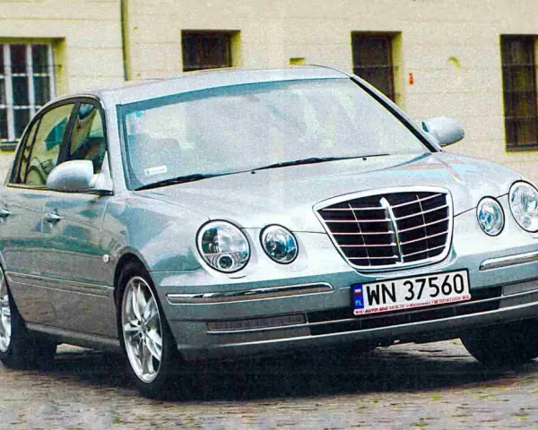 Srebrny Kia Opirus z polskimi tablicami rejestracyjnymi WN 37560 na brukowanej ulicy.