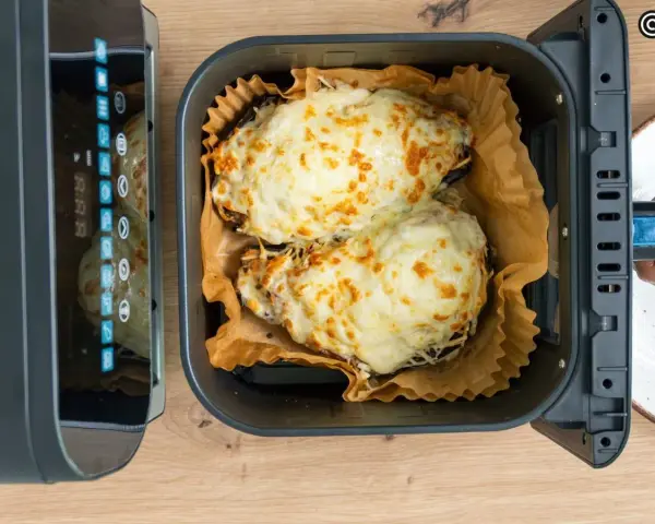 Dos mitades de berenjenas gratinadas con queso fundido, listas para disfrutar, recién salidas de la freidora de aire.