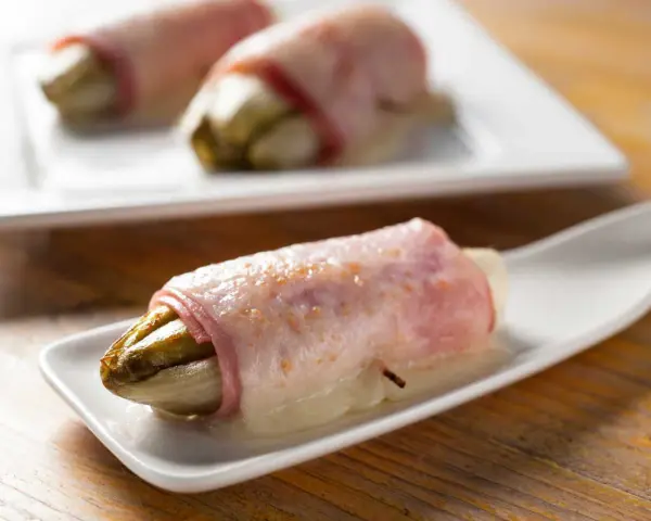 Endives au jambon sans béchamel, une recette simple et savoureuse. L'endive fondante enroulée de jambon sur une cuillère blanche.