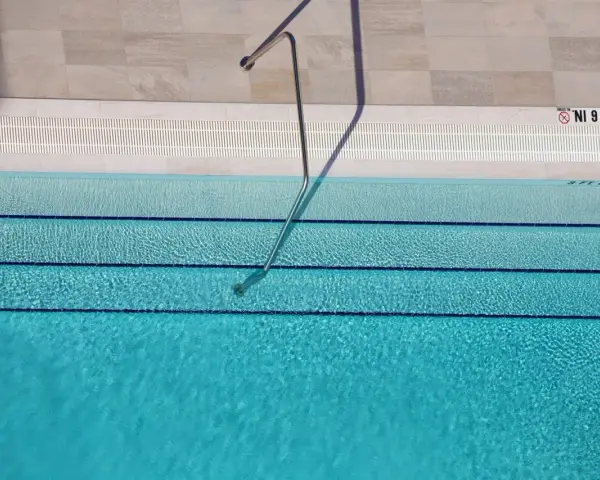 Escalera metálica en piscina de agua clara, con marcas de profundidad. El mantenimiento de piscinas es clave para su disfrute.