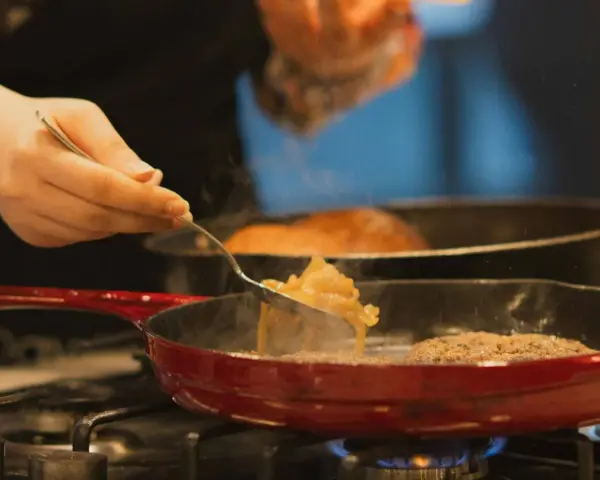 Cebolla caramelizada siendo removida con un tenedor en una sartén roja sobre el fuego.