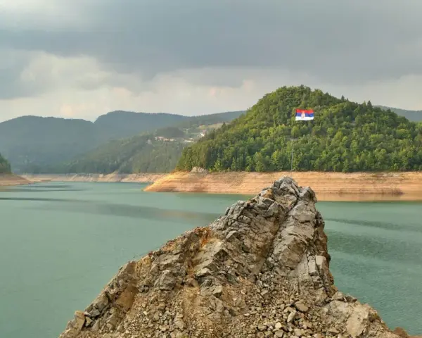 Serbska flaga na skale nad jeziorem. Krajobraz zachęca do podróży, a pytanie "czy Serbia jest bezpieczna dla turystów" wydaje się nie mieć znaczenia w obliczu tego spokoju.