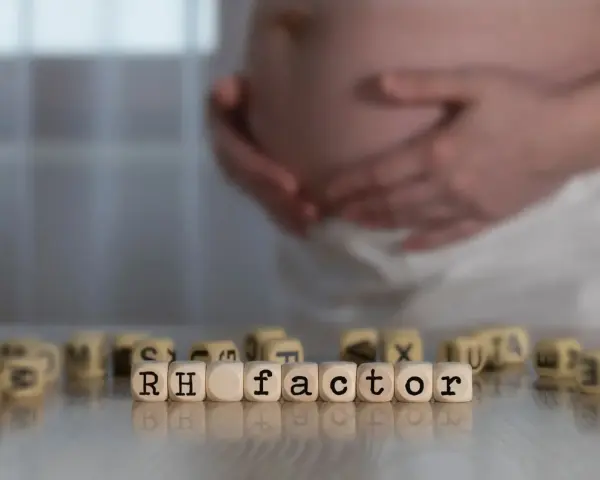 Ciąża i czynnik Rh. W tle brzuch kobiety, na pierwszym planie kostki z napisem "RH factor". Immunoglobulina w ciąży może być kluczowa.
